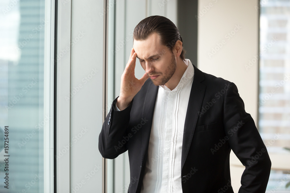 Man in formal wear standing with eyes closed touching temple because of head pain, dizziness. Businessman feels headache, recalling bad memories. Entrepreneur suffers from fatigue, overwork in office Man in formal wear standing with eyes closed touching temple because of head pain, dizziness. Businessman feels headache, recalling bad memories. Entrepreneur suffers from fatigue, overwork in office