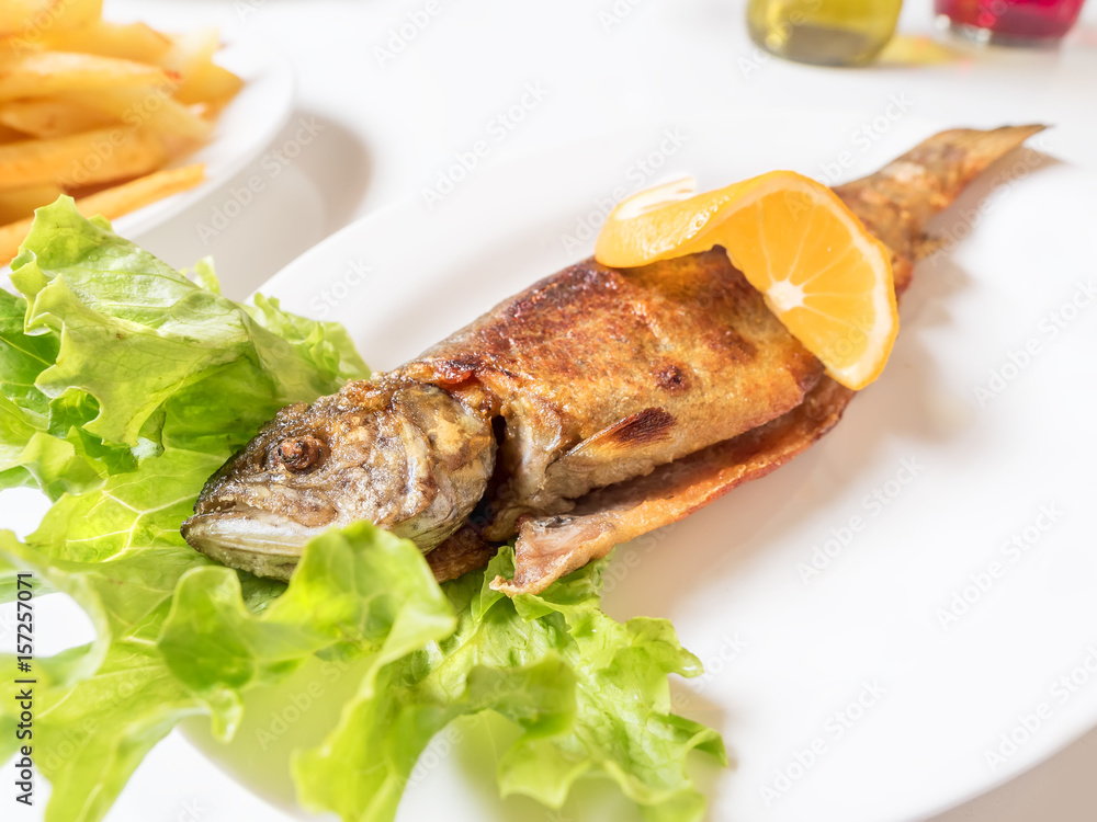 Grilled trout with orange lemon, salad leaves and french fries on white plate Grilled trout with orange lemon, salad leaves and french fries on white plate