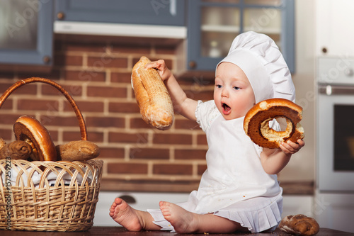 Funny little cook in kitchen with bakery. Basket with loafs a bread and bagels photo