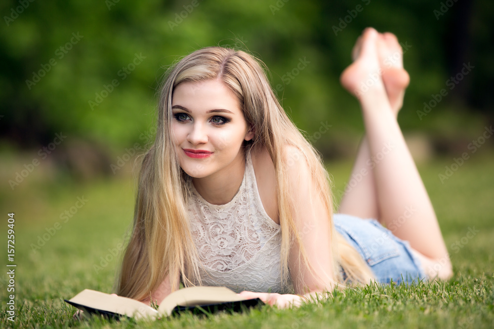 Female blonde teenager in the park with a book.