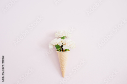 Waffle cone with white carnation bouquet on pale pastel pink background. Flat lay, top view © Floral Deco