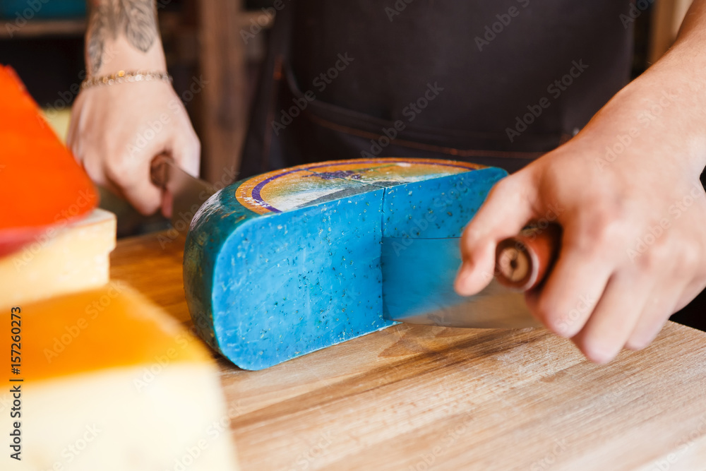 Cutting gouda pesto blue cheese in grocery shop Cutting gouda pesto blue cheese in grocery shop