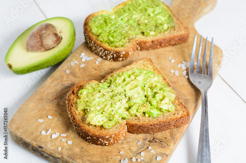 Healthy avocado toast with spices on whole wheat bread with fork and avocado