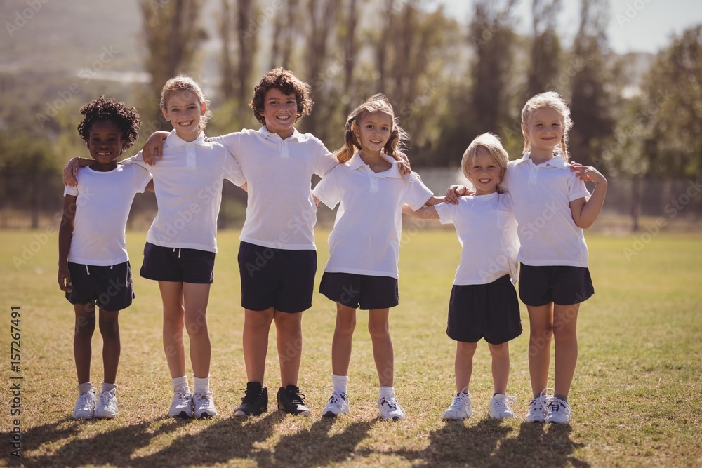 Obraz premium Portrait of happy schoolgirls standing with arms around in park