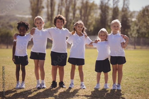 Portrait of happy schoolgirls standing with arms around in park