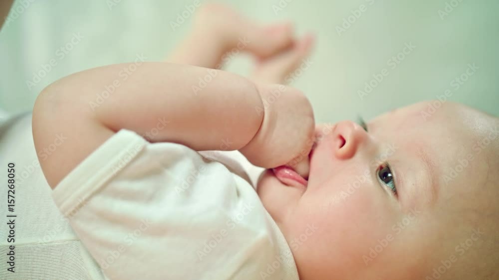 Baby's lying on a soft linen in bed at home, eating its finger. Soft focus, close-up macro shot Baby's lying on a soft linen in bed at home, eating its finger. Soft focus, close-up macro shot