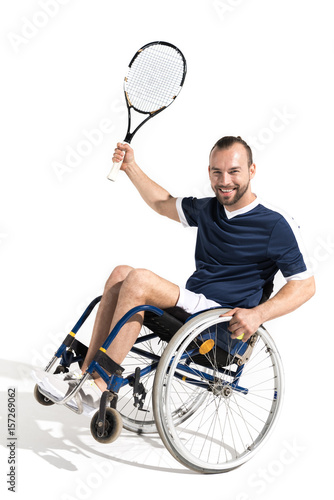 Happy young sportsman in wheelchair holding tennis racquet and smiling at camera