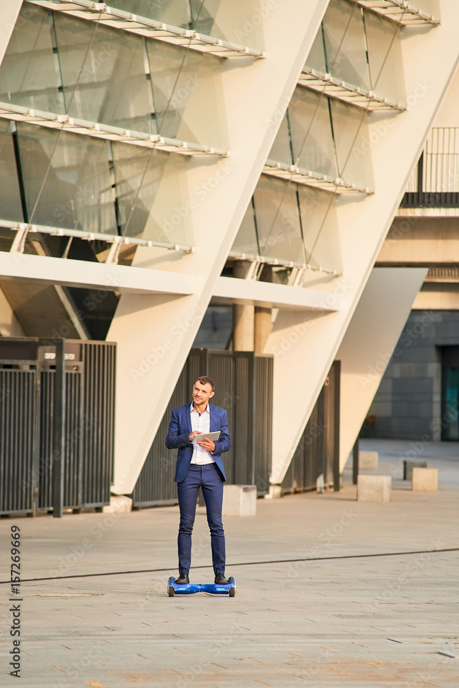 Businessman on hoverboard with tablet. Man in a suit outdoors. Businessman on hoverboard with tablet. Man in a suit outdoors.