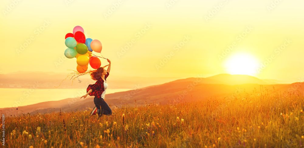 Happy cheerful girl with balloons running across meadow at sunset in summer - obrazy, fototapety, plakaty 