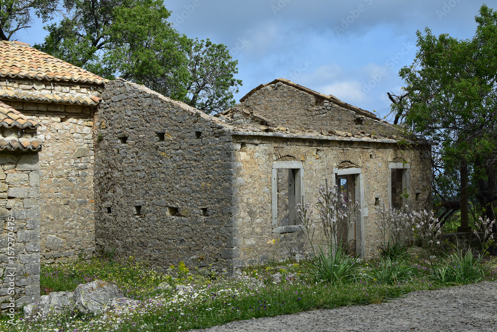 The old abandoned stone-built village of Perithia high in Pantokrator Mountain, Corfu Island, Greece. Nostalgic spring day. Clouds creep over the mountain slopes around