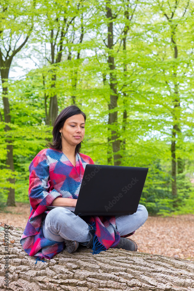 Woman sits with laptop on tree in forest Woman sits with laptop on tree in forest