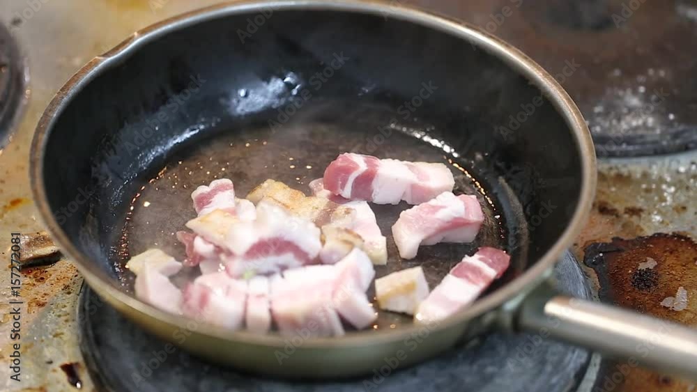 Pieces of bacon are fried in a frying pan, in the kitchen, close-up Pieces of bacon are fried in a frying pan, in the kitchen, close-up