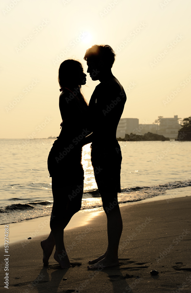 夕焼けのビーチでキスするカップル