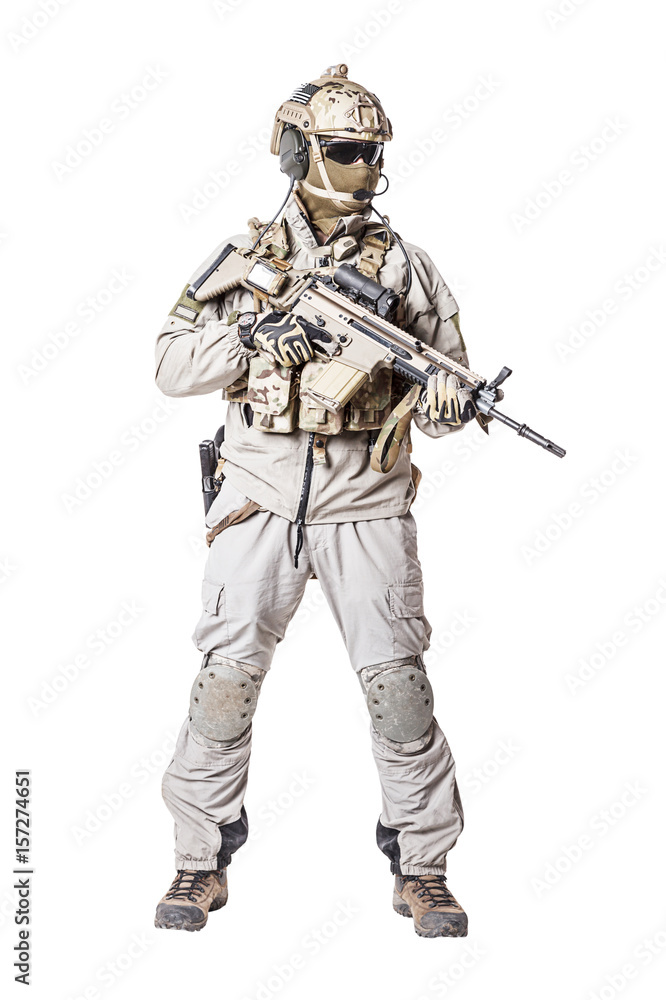 Army soldier in Protective Combat Uniform holding Special Operations Forces Combat Assault Rifle. Knee pads, mag recovery pouch, chest rig, military boots. Studio shot, isolated on white background