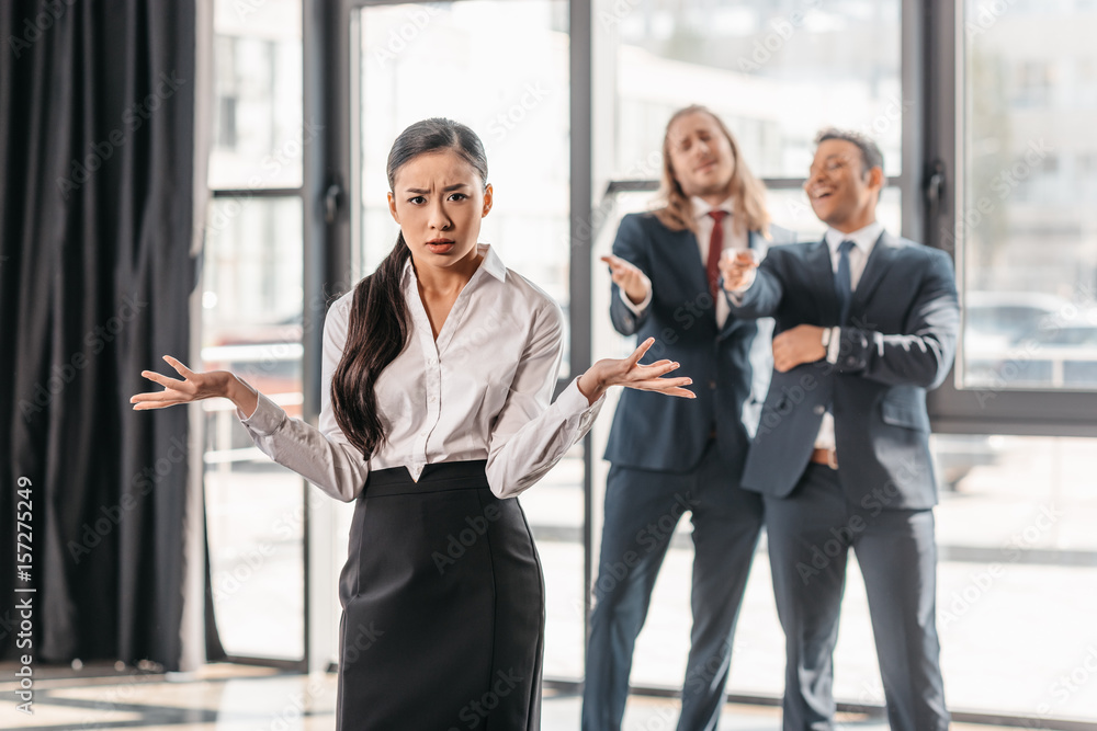 businesswoman with shrug gesture, businessmen standing behind and laughing businesswoman with shrug gesture, businessmen standing behind and laughing