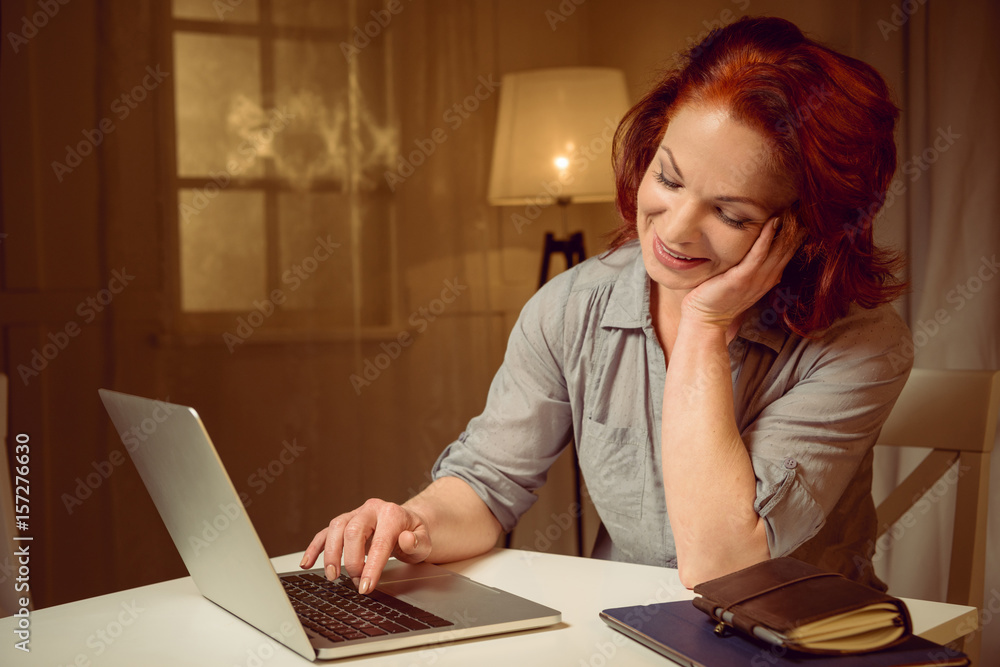 mature red hair woman working on laptop while sitting at table at home mature red hair woman working on laptop while sitting at table at home