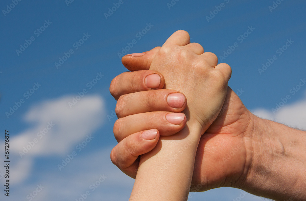 Handshake of a child and an adult against a blue sky Handshake of a child and an adult against a blue sky