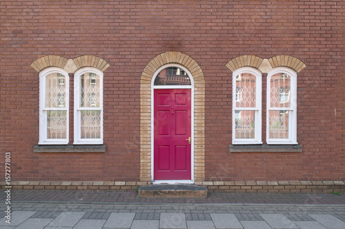 Pink door with white windows and brick wall