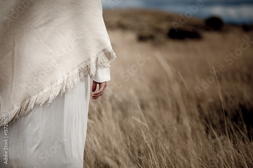 Jesus Christ's hand hangs next to his side while standing in a wheat field