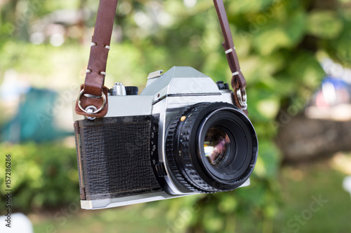 old film camera hanging by brown leather strap on natural background