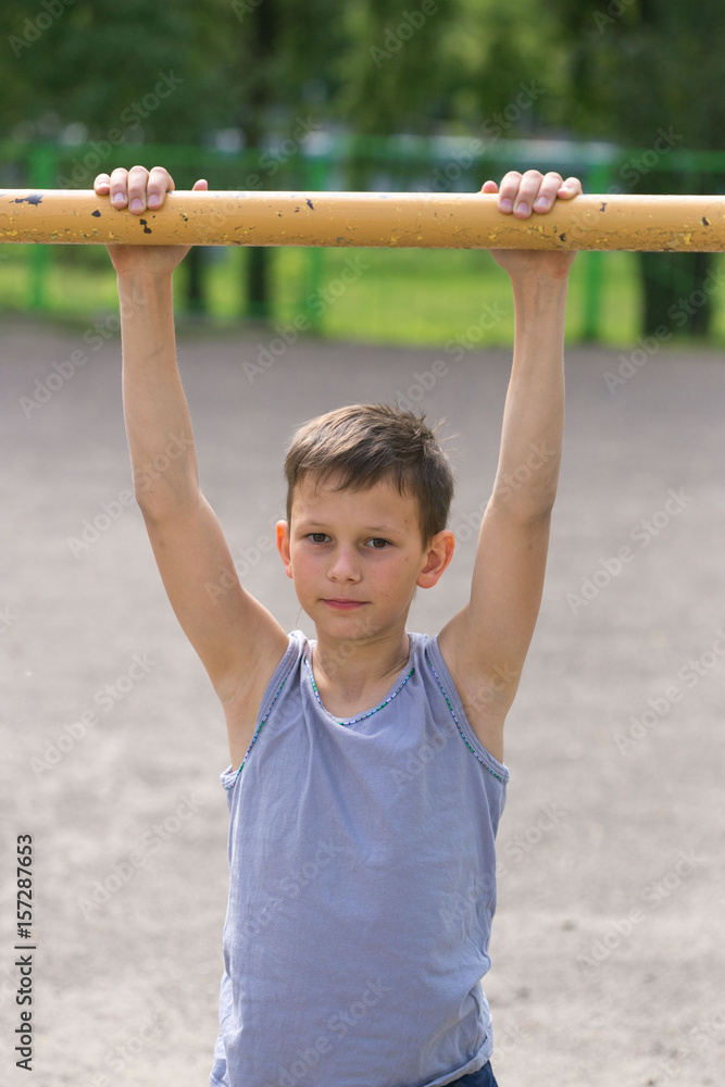Fototapeta premium A teenager in a T-shirt is engaged in gymnastics on a horizontal bar