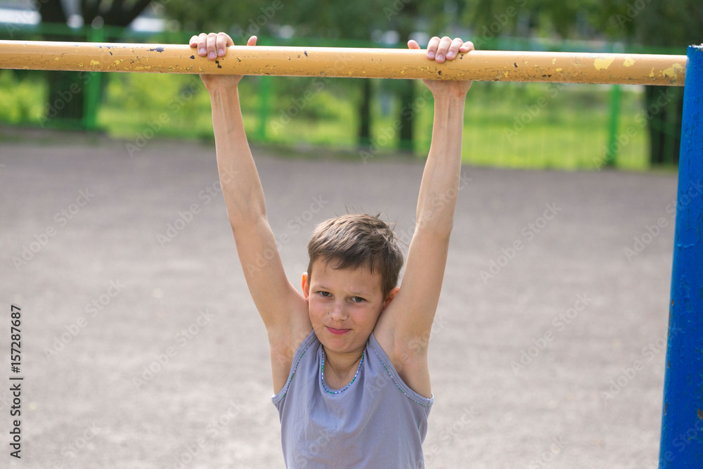 A teenager in a T-shirt is engaged in gymnastics on a horizontal bar A teenager in a T-shirt is engaged in gymnastics on a horizontal bar