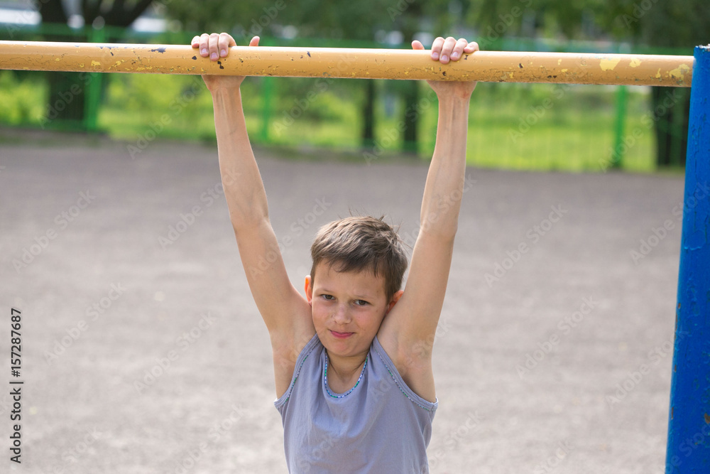 A teenager in a T-shirt is engaged in gymnastics on a horizontal bar