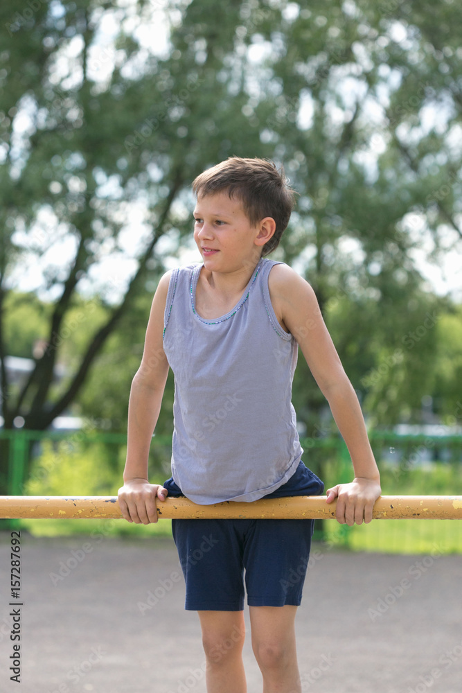 A teenager in a T-shirt is engaged in gymnastics on a horizontal bar