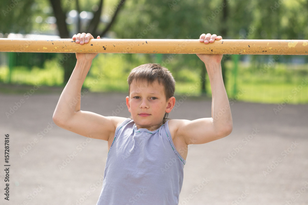 A teenager in a T-shirt is engaged in gymnastics on a horizontal bar A teenager in a T-shirt is engaged in gymnastics on a horizontal bar