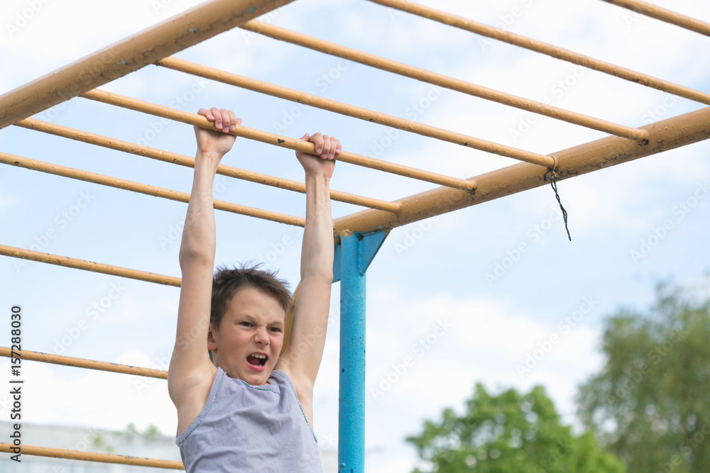 Fototapeta premium A teenager in a T-shirt is engaged in gymnastics on a horizontal bar