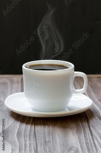 White cup of coffee on wooden surface on dark background