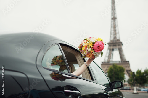 Bride reaches out hand with wedding bouquet from a car before Eiffel Tower