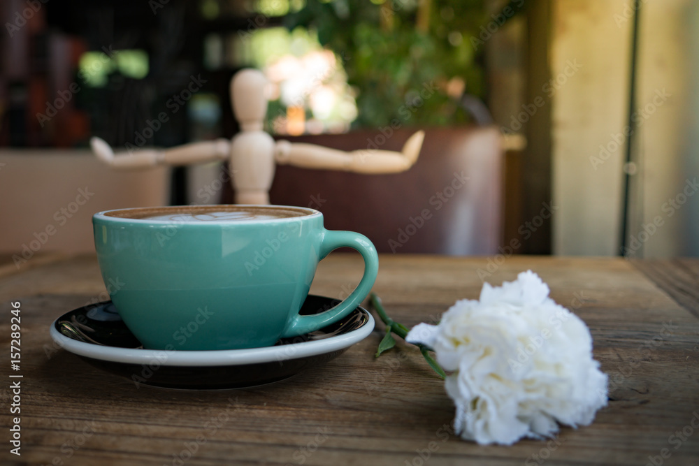 Hot mocha coffee or capuchino with white carnation flower and wood man on the wooden table Hot mocha coffee or capuchino with white carnation flower and wood man on the wooden table