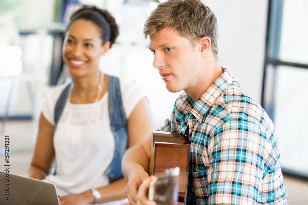 Students sitting on the floor with one playng guitar Students sitting on the floor with one playng guitar