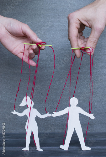 Manipulating concept, hands holding paper marionettes on the dark background. photo