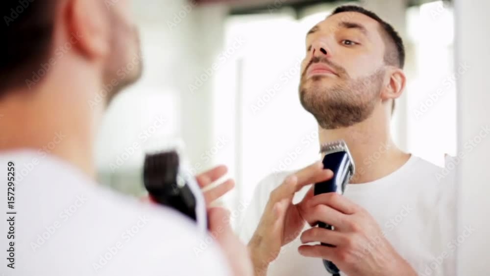 man shaving beard with trimmer at bathroom man shaving beard with trimmer at bathroom