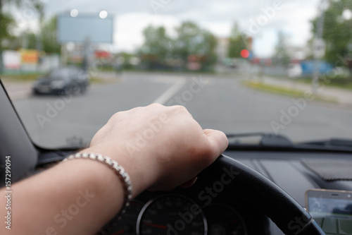 Male hand on the steering wheel while the car is in motion in city.