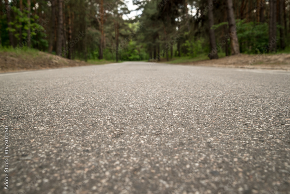 Background, the texture of gray asphalt, leaving in the distance and surrounded by forest, on the whole frame. Horizontal frame Background, the texture of gray asphalt, leaving in the distance and surrounded by forest, on the whole frame. Horizontal frame