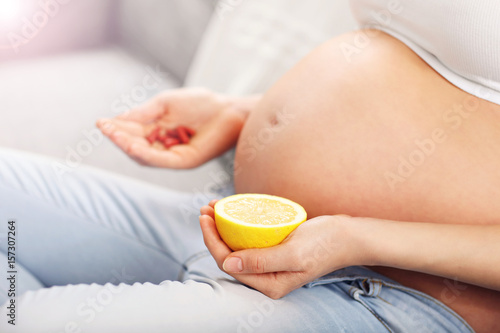 Pregnant woman holding pills and lemon at home