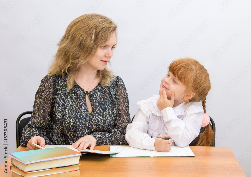 The little girl at the table with exercise books and textbooks, looking at mother The little girl at the table with exercise books and textbooks, looking at mother