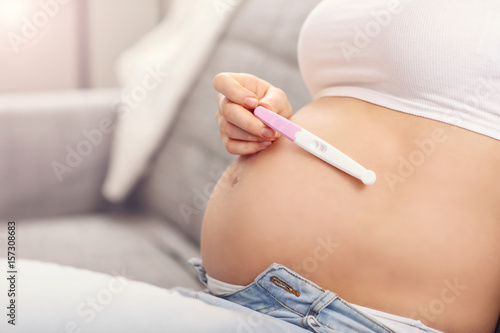 Happy pregnant woman resting on sofa with pregnancy test