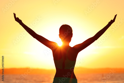 Freedom woman with open arms silhouette in sunrise against sun flare. Morning yoga girl practicing sun salutation outdoors. Carefree person living a free life. Success freedom happy life concept.