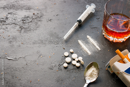 Fotografie Alcohol in a glass, drugs, syringe, pack of cigarettes on a black background with space for text