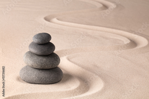 balancing a stack of black hot stones for spa wellness therapy. Zen meditation rock andsand garden. A yoga background.