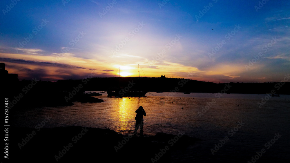photographer taking photo of the boat, sunset in Mellieha, Ghadira, Malta