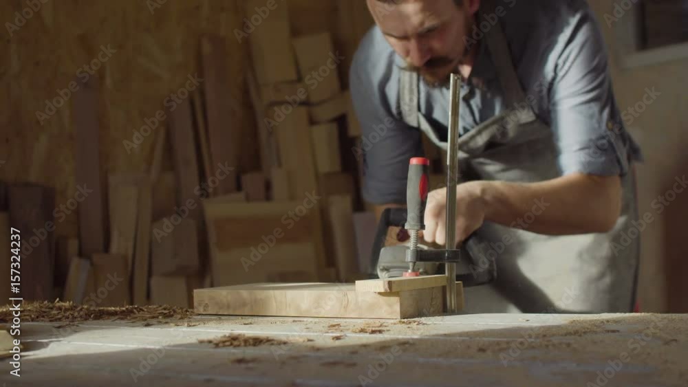 20s bearded woodworker works with brashing machine at sunny day in workshop 20s bearded woodworker works with brashing machine at sunny day in workshop