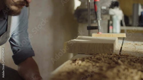 20s bearded woodworker using brashing machine tool and checking quality of work photo