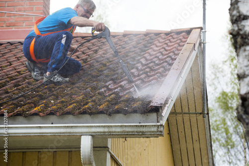 Caucasian man is washing the roof with a high pressure washer. He is wearing safety harness on a slippery roof. photo