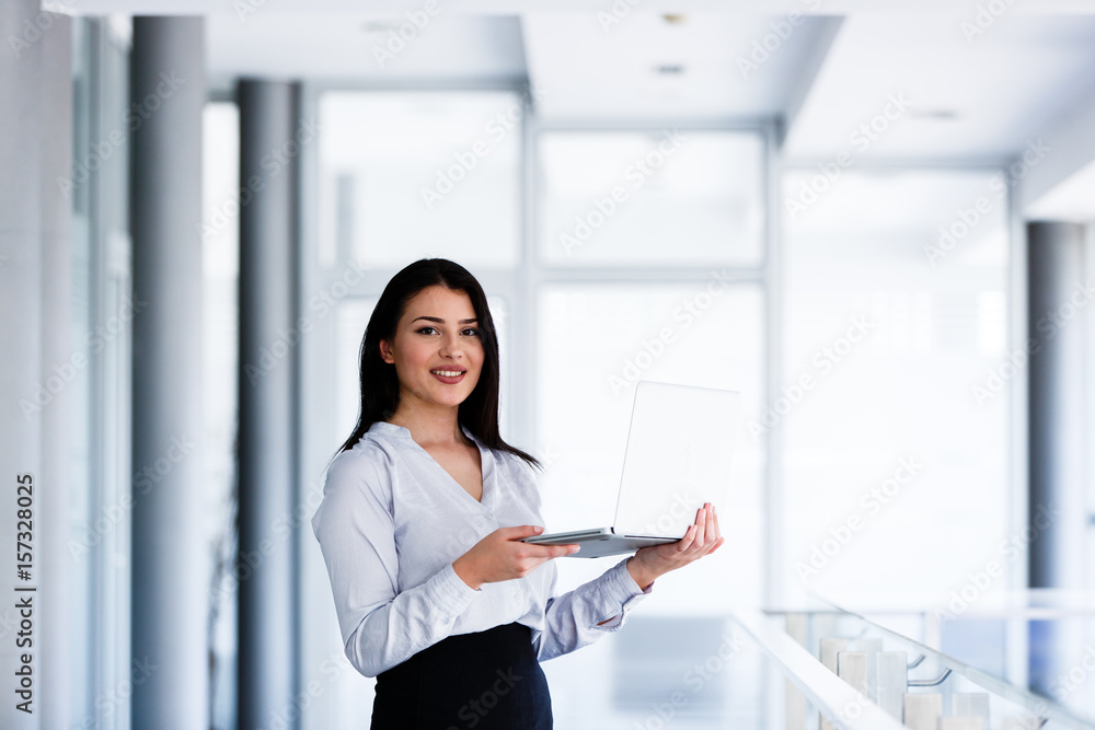 Successful woman staning in office holding laptop in her hands Successful woman staning in office holding laptop in her hands