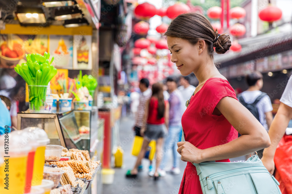 Woman tourist at chinese market Wangfujing, food street on Asia travel. Traditional Beijing snacks at outdoor market place. Asian woman looking at restaurant or outside store.